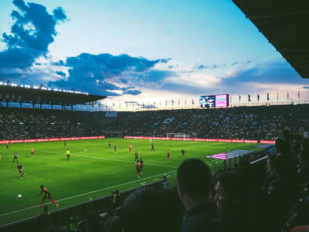Stadium filled with football fans watching a live match at sunset, with teams competing on a lush green pitch, relevant for Andorra vs England football standings and match analysis.

