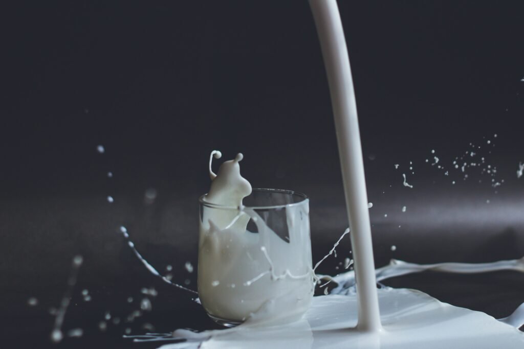 Milk being poured into a glass, creating a dynamic splash with milk droplets and overflow on a dark background, representing the freshness and appeal of semi skimmed milk in the UK